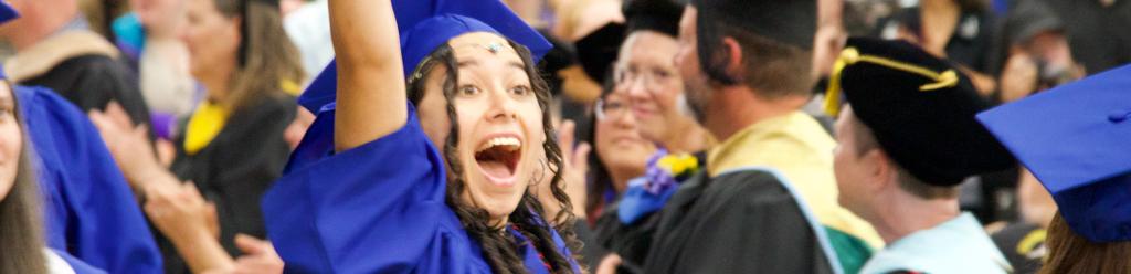 A graduating student in blue cap and gown, waves excitedly to her family